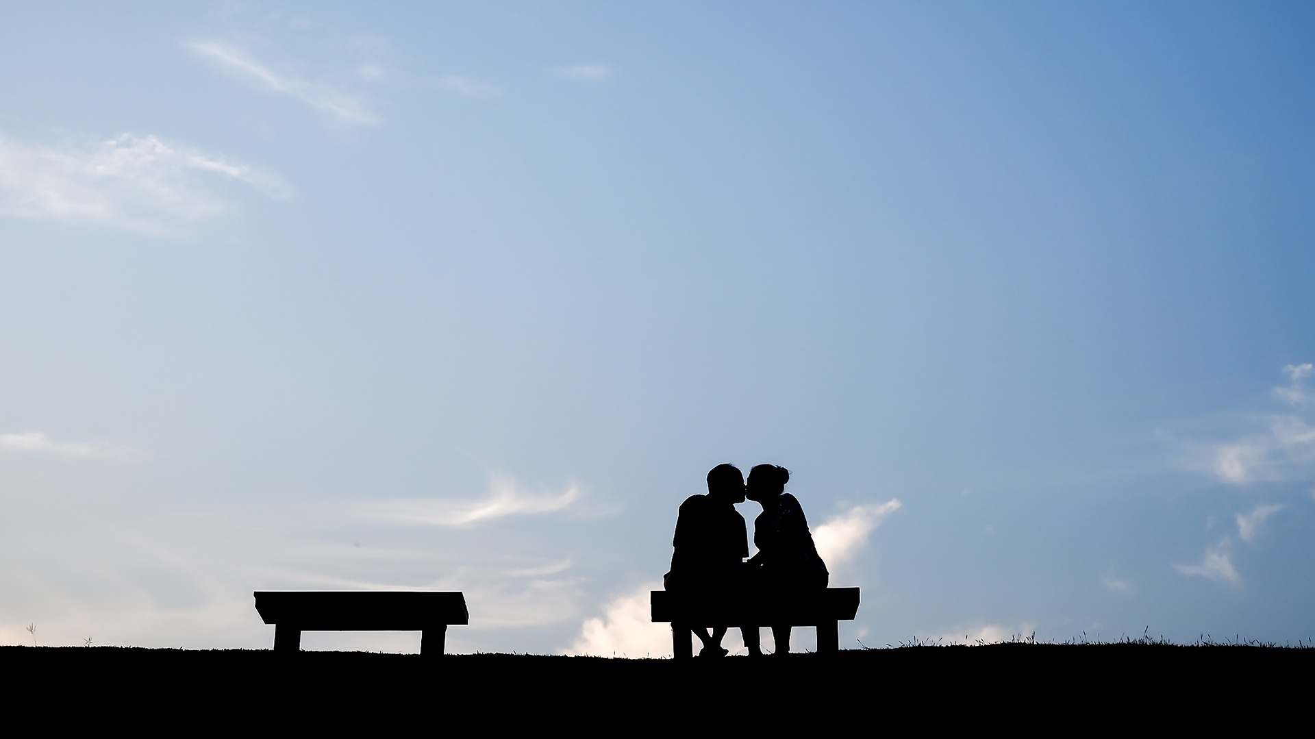 青空の下でベンチに座りキスする男女